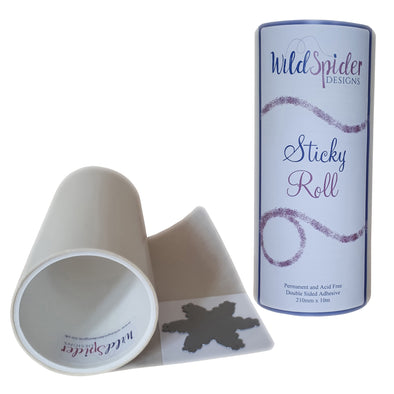 Sticky Roll stood upright showing its label along side another double sided adhesive Sticky Roll laying flat, partially unwound  with a piece of card laying on it with a die on top.